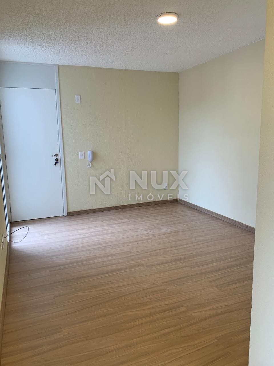 Sala ampla com piso laminado, porta de entrada e interfone