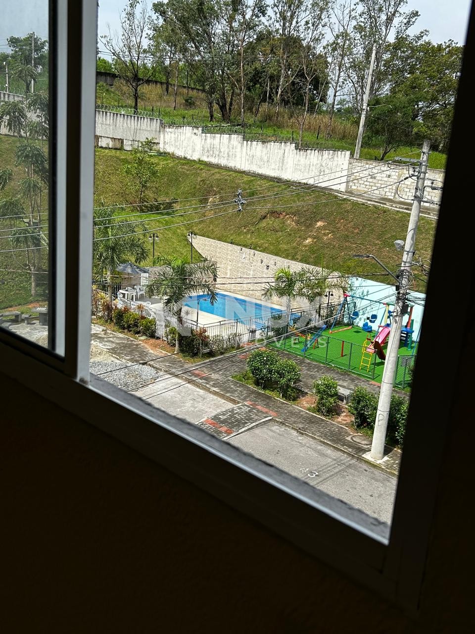 Vista da janela para a área de lazer do condomínio, com piscina e playground